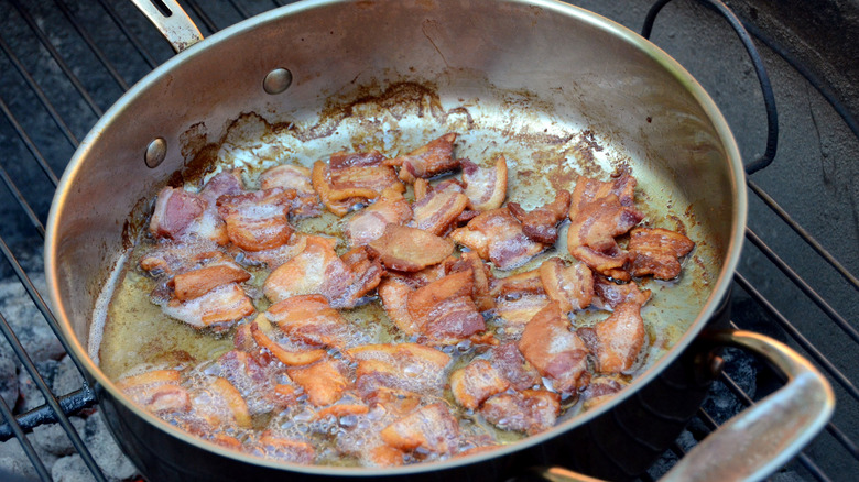 bacon cooked in frying. pan on grill