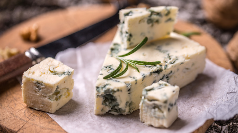 Wedge of blue cheese with cubed pieces at right and a small sprig of rosemary above them