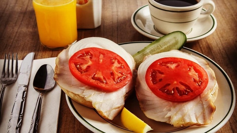 A bagel topped with smoked sturgeon and fresh tomato next to a glass of orange juice and coffee at Barney Greengrass