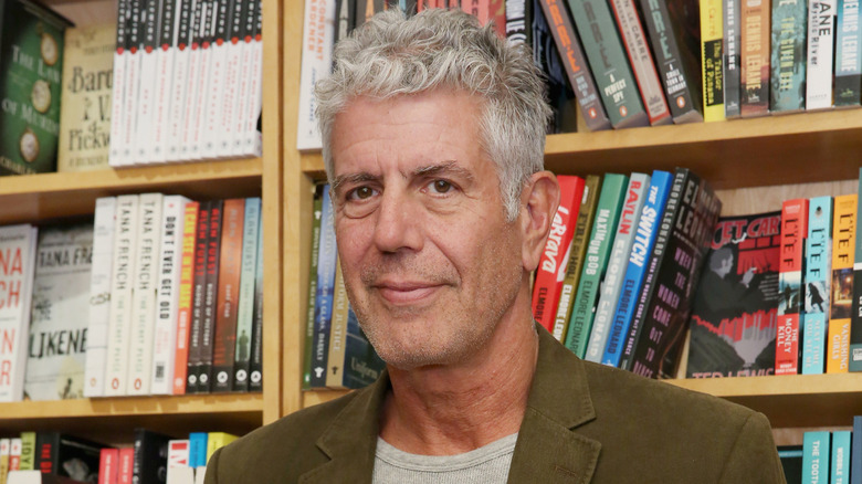 Anthony Bourdain smiles in front of shelves of books