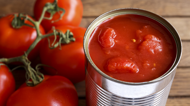 A can of tomatoes next to a bunch of fresh tomatoes