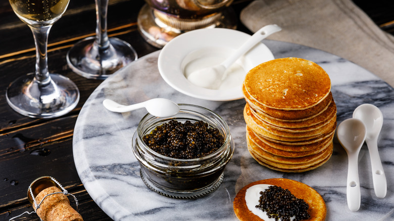 Caviar on a plate with blinis next to wine glasses