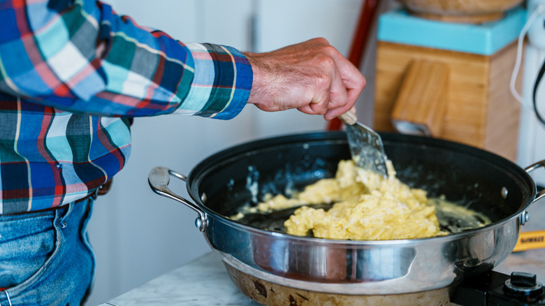 person cooking scrambled eggs in pan