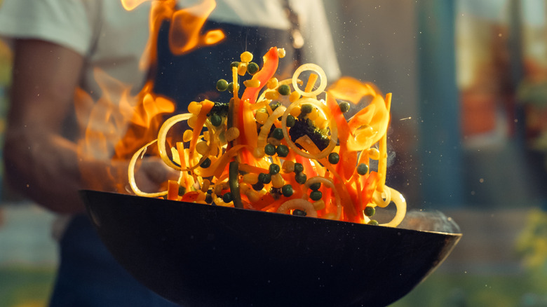 A chef tosses a fiery stir-fry in a wok