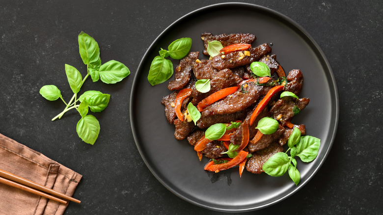 A beef stir-fry rests in an elegant black bowl next to fresh basil