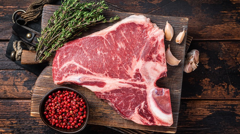 raw porterhouse on chopping board with herbs