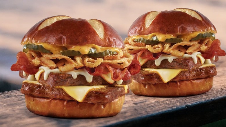 Two Wendy's Pretzel Bacon Pub Cheeseburgers sit on a wooden surface in an outdoor setting.