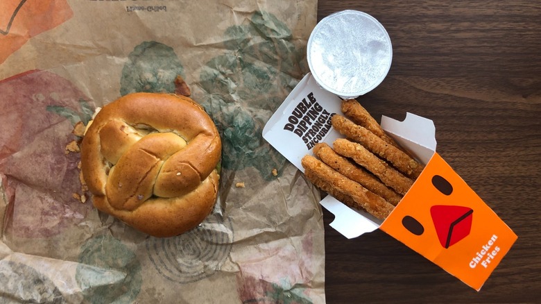 A Burger King burger with a pretzel bun sits near a container of Chicken Fries