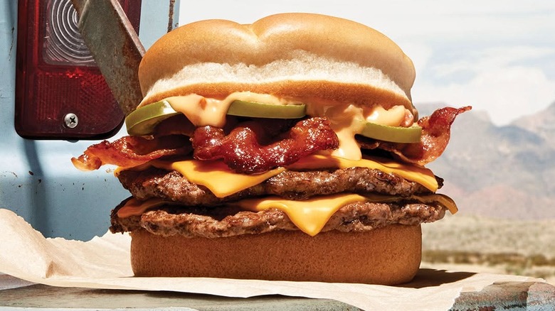 An A&W Jalapeño Queso Bacon Double Cheeseburger sits on the tailgate of an old pickup truck in an outdoor setting.