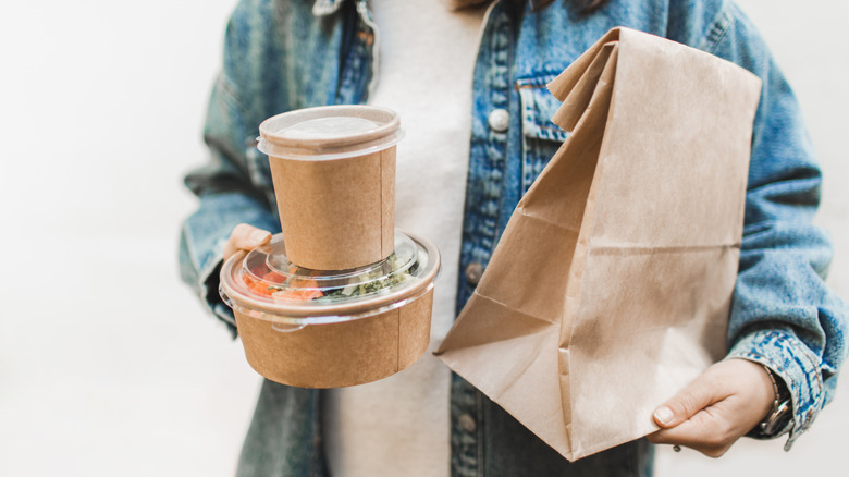 A woman in a denim jacket holds three containers of takeout food
