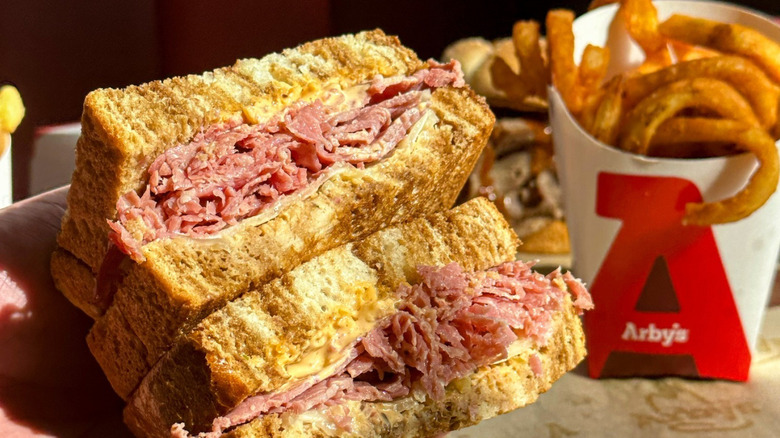 A hand holds a reuben sandwich from Arby's