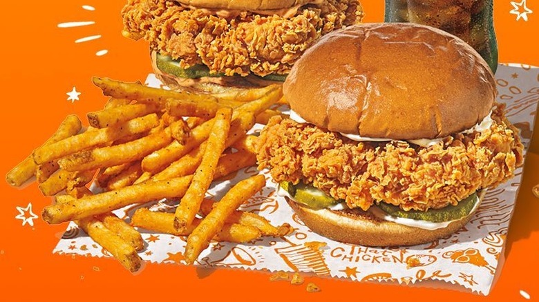 Two chicken sandwiches from Popeyes sit on a wrapper with fries