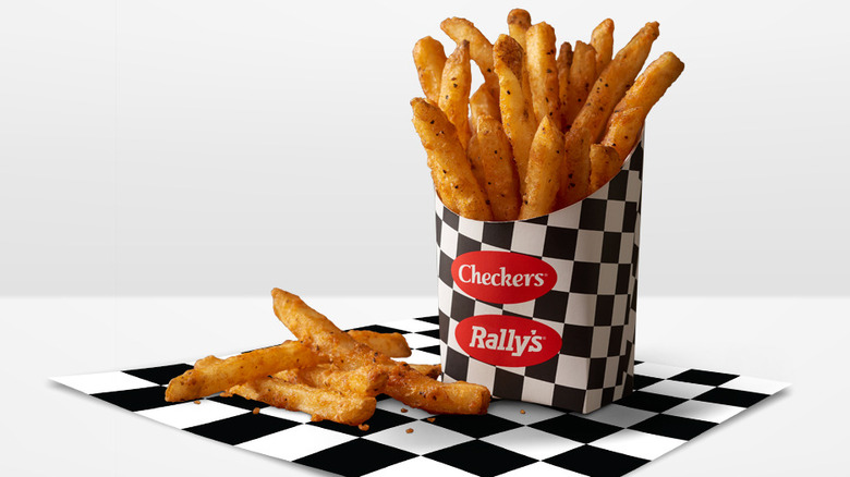 A container of Checkers and Rally's french fries on a black-and-white square of checkered paper, with a few fries lying outside the container