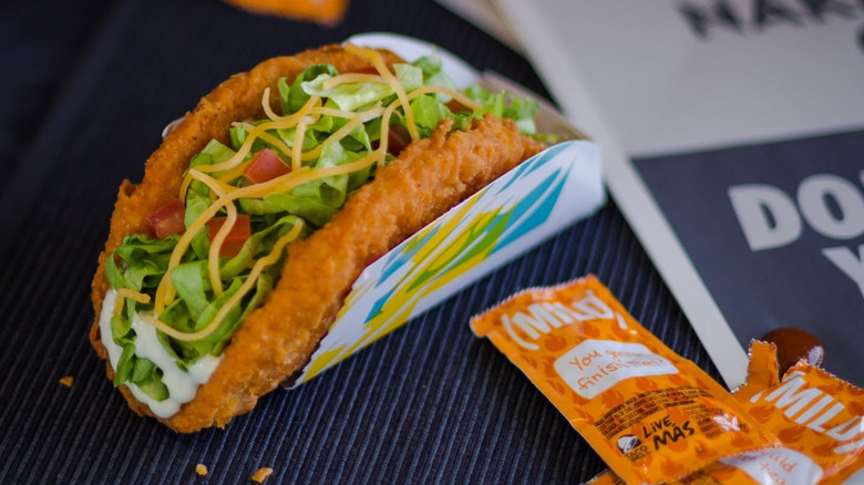 A naked Chicken Chalupa sits next to some hot sauce packets.