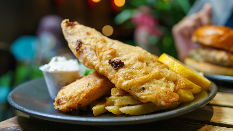Plate of fish and chips with a sandwich in the background