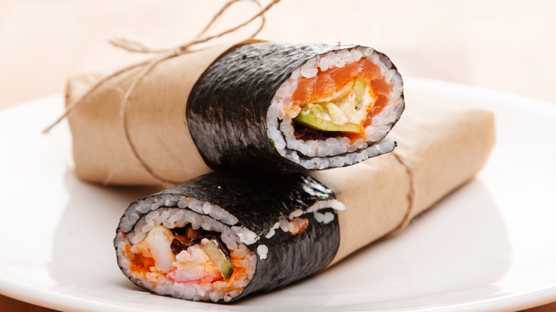 Two sushi burritos in brown parchment paper on white plate