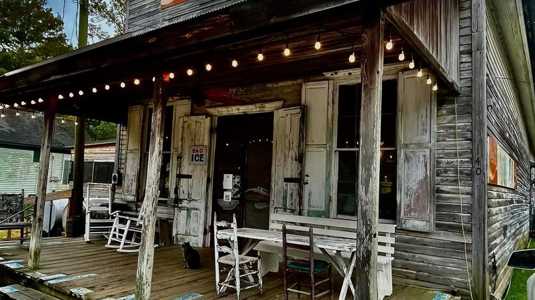 A weathered wooden building, wooden table and chairs on the porch, shutters on the window