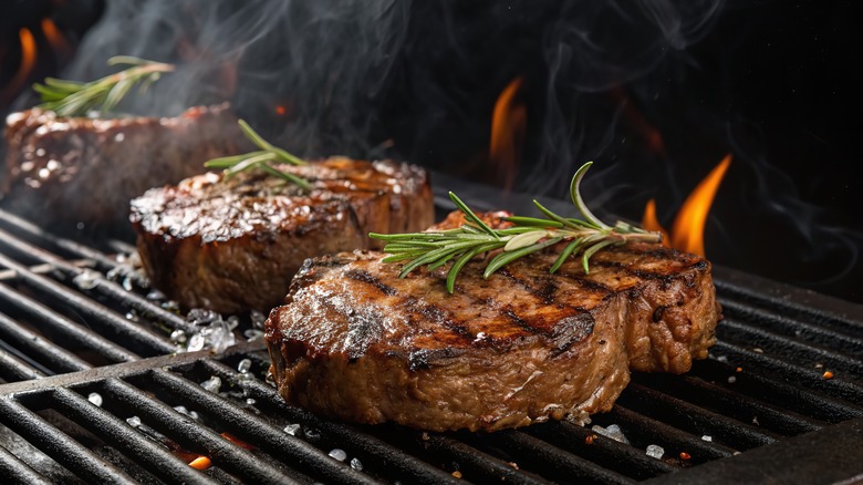 Three steaks grilling with rosemary and salt
