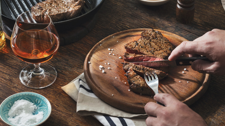 A man eating a steak dinner with a glass of cognac