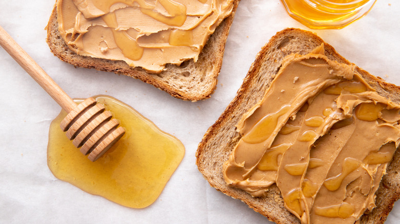 Two slices of bread with peanut butter and a honey spoon