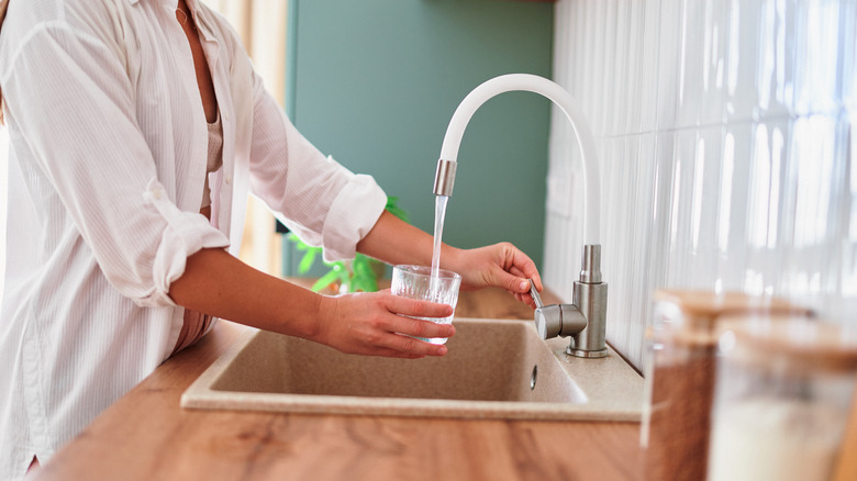 A person filling a glass in a sink