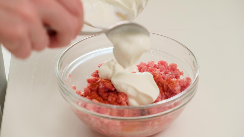 Chef adding a dollop of sour cream to raw ground beef