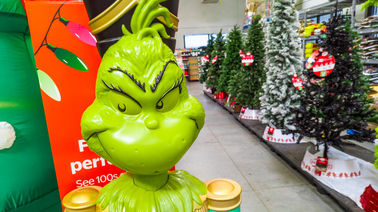 A Grinch decoration in front of a festive Christmas tree aisle in a Walmart