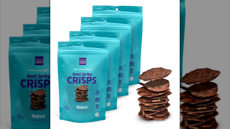 Four packages of Naked Beef Jerky Crisps are lined up next to a stack of jerk crisps, against a white background