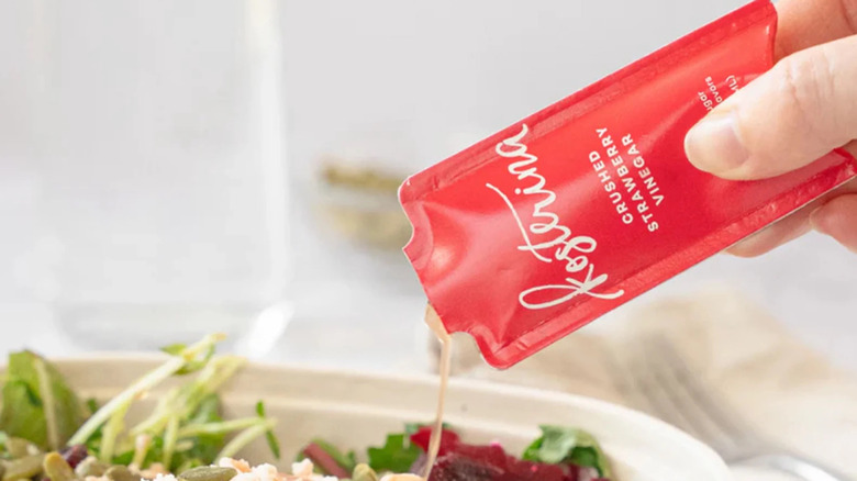 A hand drizzles Kosterina Crushed Strawberry Vinegar over a salad
