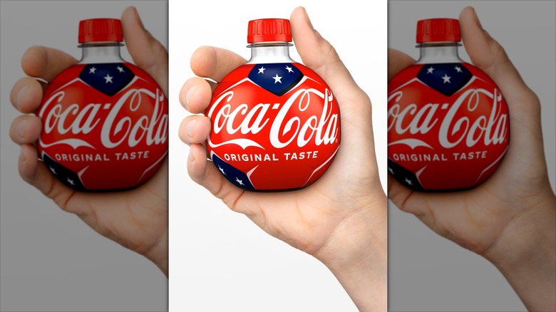 A hand holds up a Coca-Cola Orb Bottle