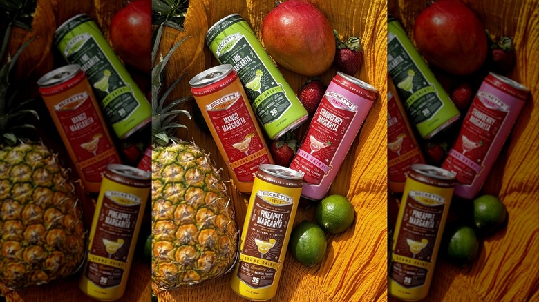 Cans of non-alcoholic margaritas lie on a blanket with some fruit.