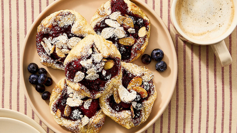 Blueberry pastries with sliced almonds made with Great Value Puff Pastry sits next to a cup of coffee.