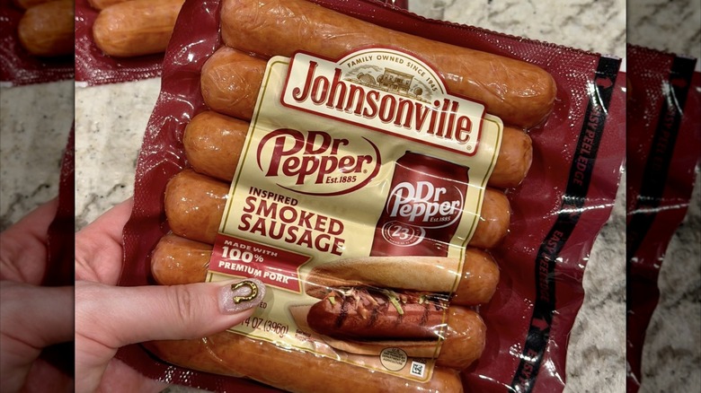 A hand holds a package of smoked sausages