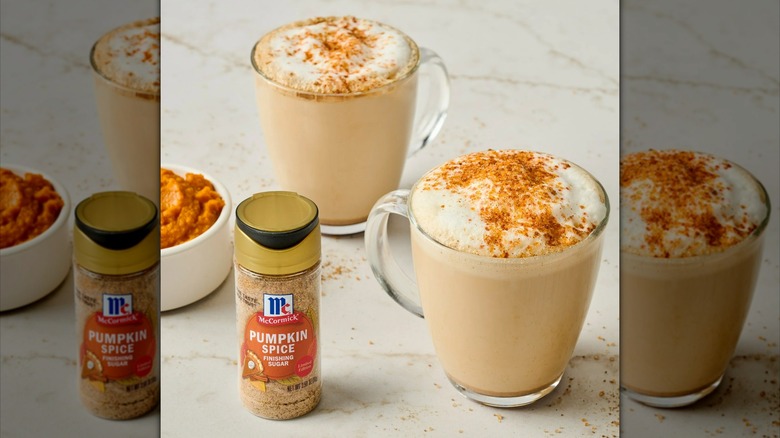 A jar of McCormick pumpkin spice finishing sugar sits near two hot drinks and a ramekin of pumpkin puree