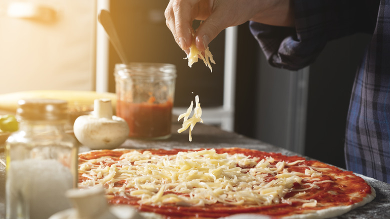 person adding cheese to homemade pizza