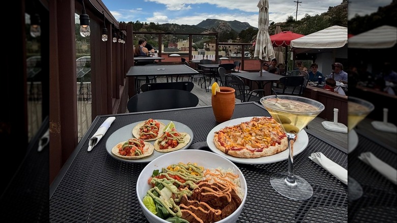 Assorted dishes on an outdoor patio table at Antler's Rooftop Tavern with mountains in the background