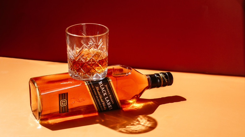A tumbler glass sits on a tipped-over bottle of Johnnie Walker.
