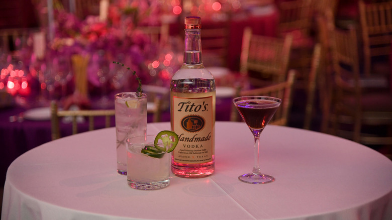 A bottle of Tito's vodka sits with cocktails on a table