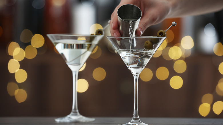 A hand pours vodka from a shot glass into a martini glass