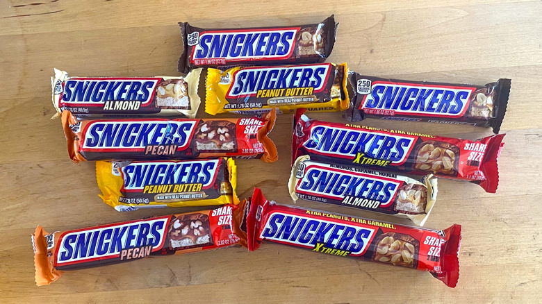 Various Snickers bars sit on a wooden surface.