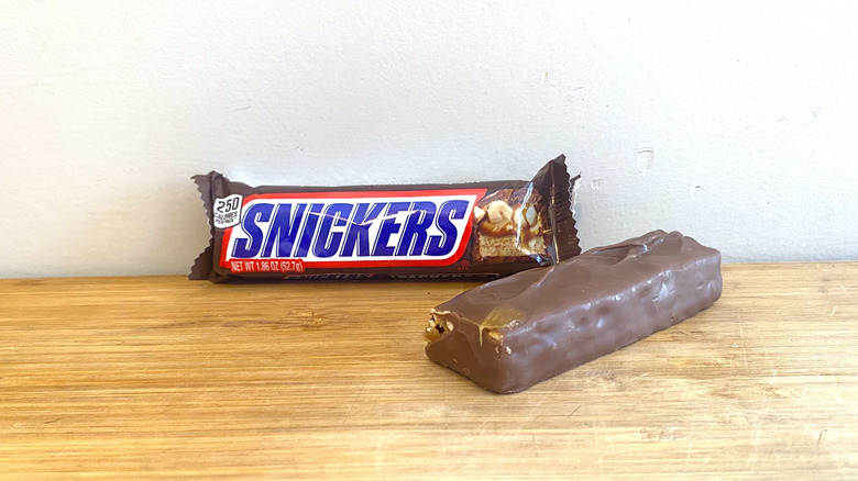 An unwrapped Snickers sits next to a wrapped Snickers.