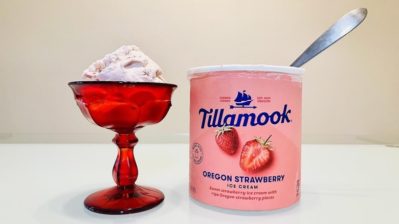 A fancy red glass bowl of Tillamook strawberry ice cream sits next to an open carton