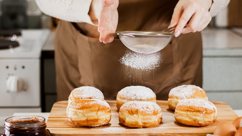 Person dusting powdered sugar on donuts