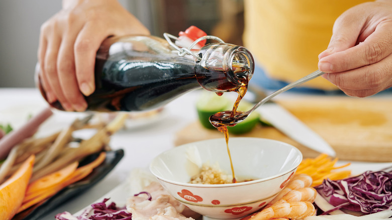 Person pouring soy sauce in a spoon over a bowl