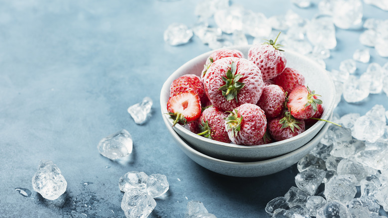Frozen strawberries sit in a bowl with chunks of ice around it