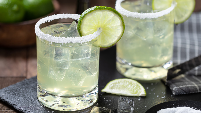Two margaritas with salt rims and limes