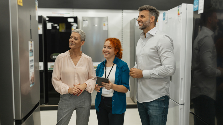 Three people examine a refrigerator in a store.