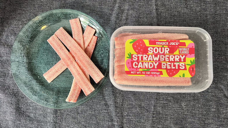 A package of Trader Joe's Sour Strawberry Candy Belts sits next to some of the candies sitting on a glass plate.