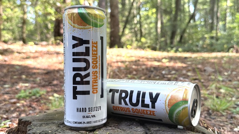 Two cans of Truly Citrus Squeeze on the next to each other, one on its side, with a forest background.