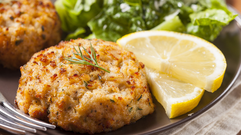 A plate of golden fried crab cakes with lemon slices and green salad